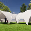 White Curved Tents in Green Grass Field With Trees and Blue Sky