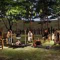 Wooded Camping Site With Campfire People Sitting Around And Natural Surroundings