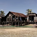 Waterfront Stilt Houses With Wooden Platform Person In Blue Ladder Buckets And Tire