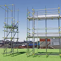 Public Facility Construction Scaffolding with Metal Frames Yellow Connectors on Green Ground and Background Buildings