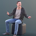 Smiling Man Sitting On Black Cube Wearing Gray Cardigan And Blue Jeans