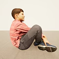 Boy Sitting on Light Floor in Pink Striped Shirt Gray Pants with Hands on Feet