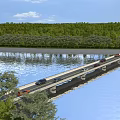 Bridge With Cars Driving Over River Surrounded By Green Trees And Grassy Banks