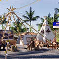Scenic Campsite With Tipi Tents Palm Trees String Lights And People Relaxing On Wooden Chairs