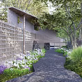 Garden Landscape Design With Perforated Stone Wall Pathway Lush Green Plants And Purple White Flowers
