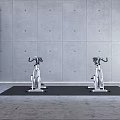 Two Stationary Exercise Bikes On Black Mat With Brick Wall And Gray Floor