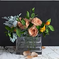 Glass Vase With Peach Roses Green Leaves Silver Foliage And Yellow Fruits On Marble Surface
