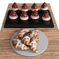 Tray Of Cupcakes With Chocolate Frosting And Plate Of Powdered Sugar Croissants On Wooden Table
