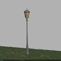 Lit Outdoor Lamp With Yellow Light Metal Pole Standing On Green Grass Against Blue Wall