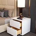 White Bedside Table with Lamp Books and Golden Ornament beside Beige Upholstered Headboard Bed