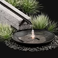 Circular Black Water Fountain With Stone Structure Green Plants And Pebbles