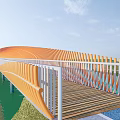 Curved Orange Landscape Bridge With White Railings And Wooden Deck Over Water In Green Surroundings