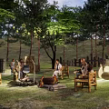 Wooded Camping Site With Campfire People Sitting Around And Natural Surroundings