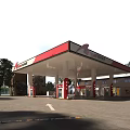 Modern Gas Station Exterior With Red White Canopy Fuel Pumps And Trees