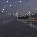 String Lights Hanging Over Wooden Boardwalk With White Railings Bridge And Water Reflection At Evening