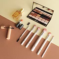 Perfume And Cosmetics Collection With Eyeshadow Palette Lipstick Brushes And Mascara On Soft Color Background