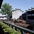 Traditional Chinese Commercial Landscape With White Walls Black Tiles Water Pond Green Plants And Pedestrians