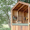 Wooden Trailer Style Cabin Surrounded by Trees with Two People Resting Outside
