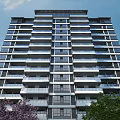 Modern High Rise Residential Building With Multiple Balconies Surrounded By Trees And Clear Sky