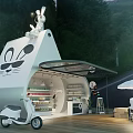 Rabbit Shaped Kiosk With Open Shelves Goods White Scooter Tables Chairs Umbrella Green Woods Road