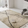 Square Beige Rug With Black Lines and Tassels in Bright Room With Chair and Blanket