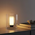 Lit Transparent Glass Table Lamp With Warm Light And Stacked Books On Tabletop