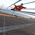 Man Sitting on Metal Pole Wearing Orange Outfit by Ocean Beach with Distant Mountains Sunset