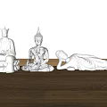 Carved Buddha Sculptures In Three Different Poses On Wooden Floor Against White Wall