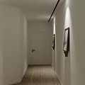White Corridor Interior With Wooden Door Paintings And Wooden Floor Ceiling Light Strips