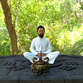 Man Sitting Cross Legged on Carved Stone Platform With Incense Burner and Lush Green Trees