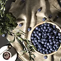 Fresh Blueberries in Wooden Bowl with Scattered Green Leaves and Linen Cloth on Dark Surface
