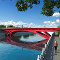 Scenic Red Bridge Over River With Pedestrians Green Trees And Blue Sky