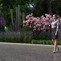 Woman Walking In Garden With Palm Trees Green Plants Purple Flowers And Cactus