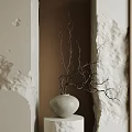 Gray Vase With Twigs On White Pedestal Against Beige And Brown Textured Walls