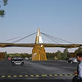 Modern Design Entrance Gate with Golden Umbrella Like Top Logo and Cars in Parking Area