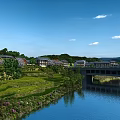 Rural Landscape With River Bridge Green Fields Houses Trees Under Blue Sky And White Clouds