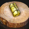 Traditional Homemade Food Wrapped in Green Leaves on Round Wooden Slice