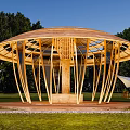 Wooden Pergola Featuring Circular Top And Radial Beams In Outdoor Grassland With Trees