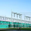 Green Industrial Factory Building With Metal Power Transmission Towers Under Blue Sky And Green Grassland