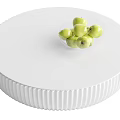 Round White Coffee Table With Ribbed Base And Glass Bowl Of Green Apples