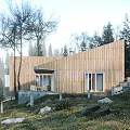 Detached Wooden House With Sloped Roof Surrounded By Trees And Stacked Wood