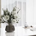 Dark Vase With White Flowers And Green Foliage On White Marble Tabletop Near Curtains