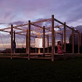 Wooden Frame Landscape Pavilion In Green Grassy Area With Surrounding Trees And People Relaxing
