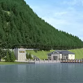 Beautiful Mountain Landscape Featuring Dense Forest Lakefront Buildings Green Grass And Blue Sky