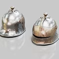 Two Antique Metal Helmets With Decorative Tops And Riveted Edges On Shiny Surface