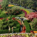Lush Park Landscape With Vibrant Flowers Green Trees Winding Path People Strolling And Wooden Bench