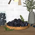 Black Fruits on Wooden Plate with Green Leaves Scattered Small Fruits Near Transparent Vase