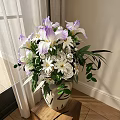 White Vase with Purple Irises White Flowers and Green Leaves on Wooden Table Near Curtain