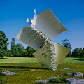 Modern Metal Sculpture Featuring Folded Sheets Spiral Structure In Outdoor Green Grassland With Trees