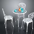 White Metal Outdoor Table With Intricate Cutout Chairs Orange Vase Blue Cups And Flower Decoration
